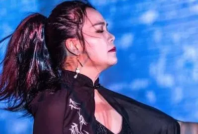 A woman wears a dark cape and has a pony tail.