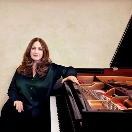 Simone Dinnerstein sits beside a grand piano.