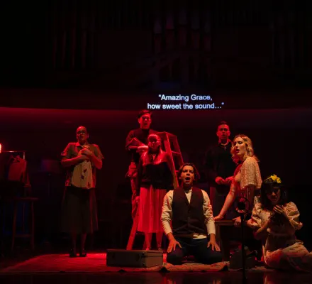 A group of students stand on stage singing. They are bathed in red light.