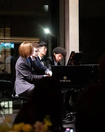 A group of four students sit together playing a grand piano