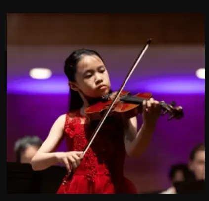 A young girl wears a red dress and places the violin.