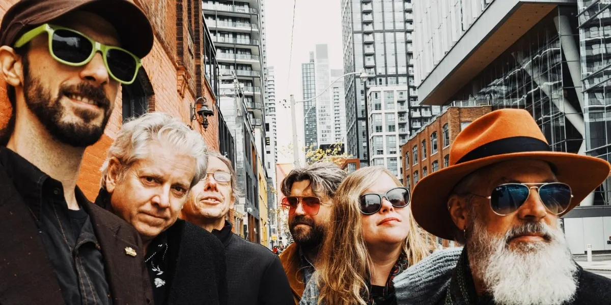 Six band members standing outside a city area with very tall buildings.
